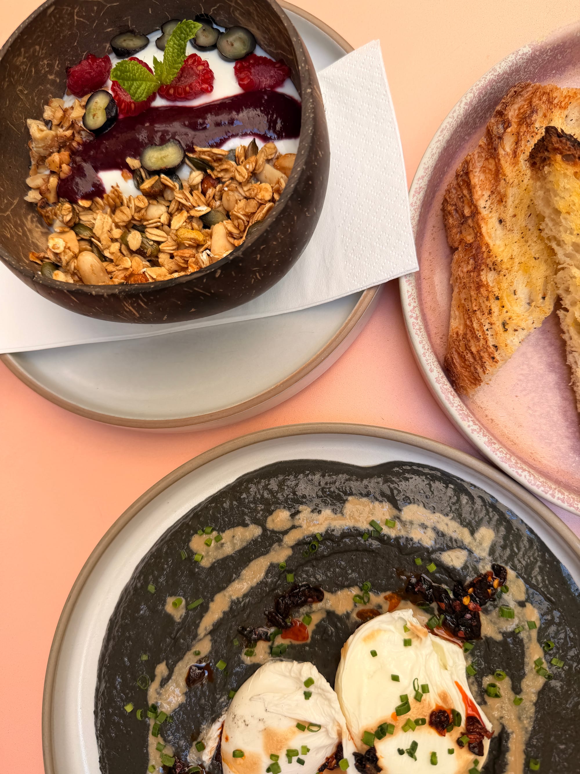 Overhead spread — smoothie bowl, sourdough toast and poached eggs on a pink table